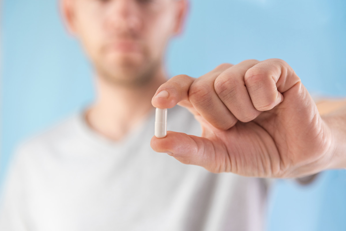 Man hold white capsule with collagen in male hand on blue background. Nutritional supplement, medicine, drug for joints protection, skin care, arthritis prevention. Selective focus